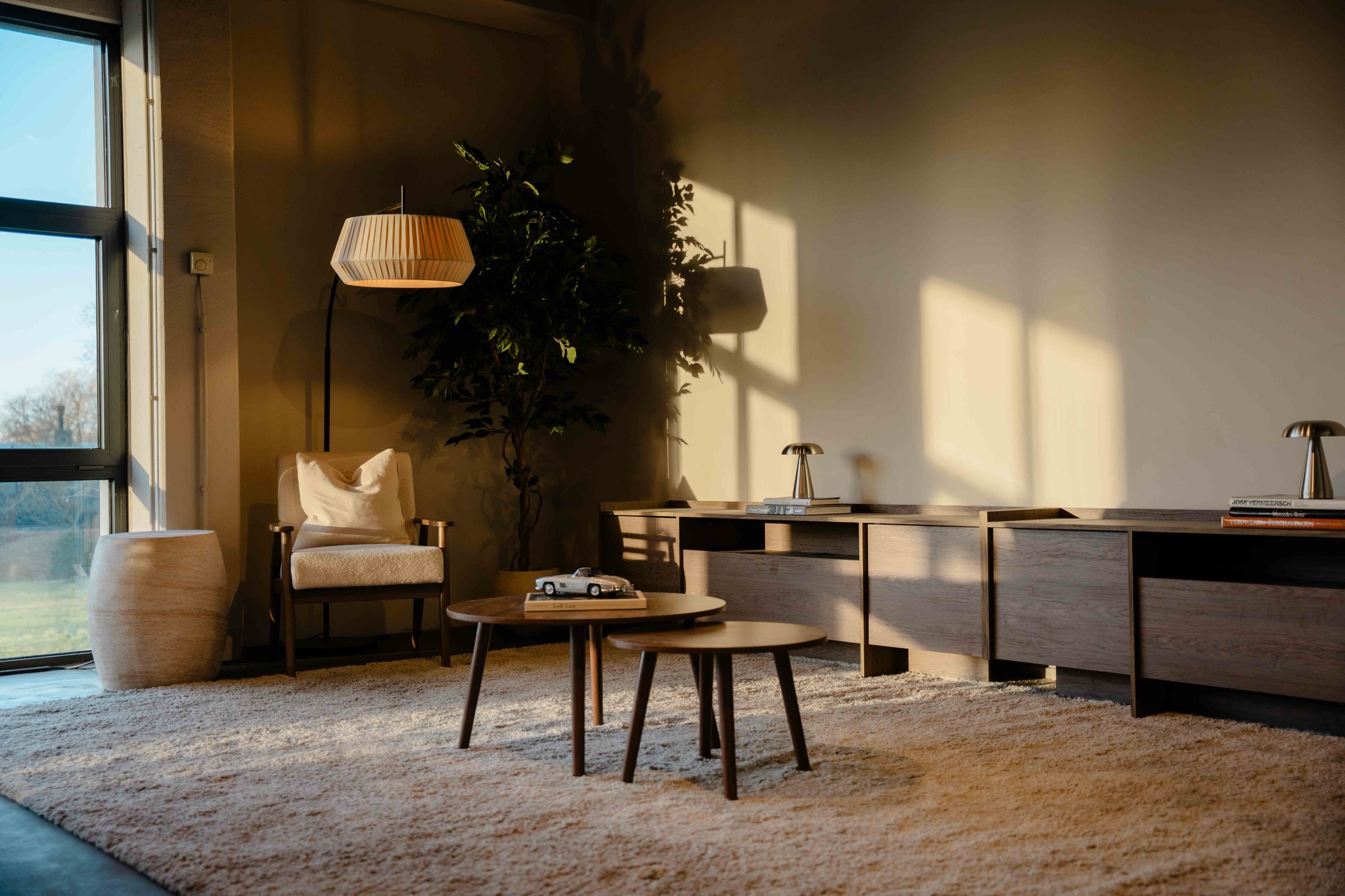 VICAR Oostkamp kantoor - lounge-hoek met boucle stoel, hangende lamp en houten salon-tafels in avondlicht